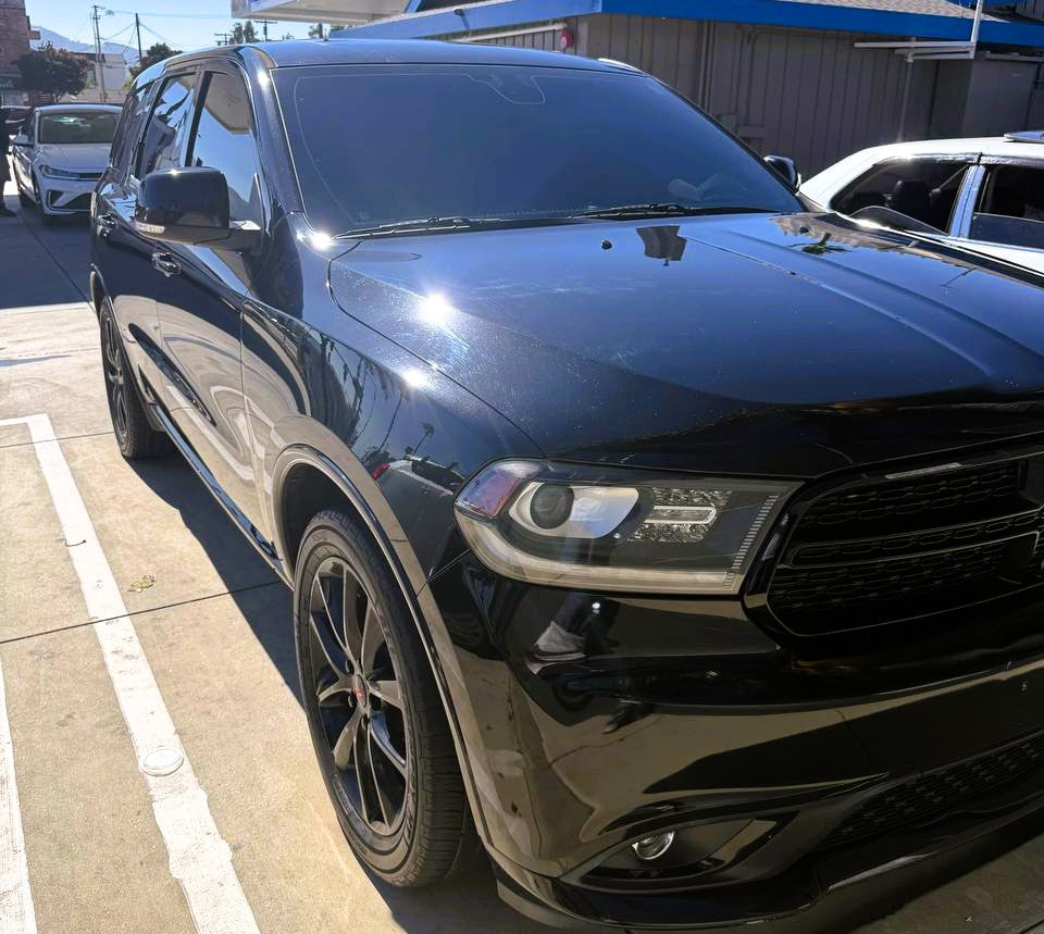 A black SUV parked in an outdoor lot near a gas station, photographed from a low front three-quarter angle under bright daylight.